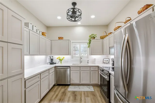 a kitchen with stainless steel appliances a sink a stove a refrigerator cabinets and a window