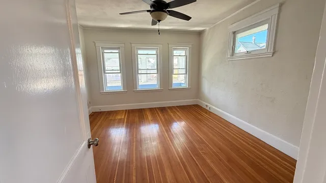 an empty room with wooden floor chandelier fan and windows