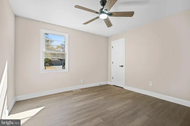 an empty room with wooden floor ceiling fan and windows