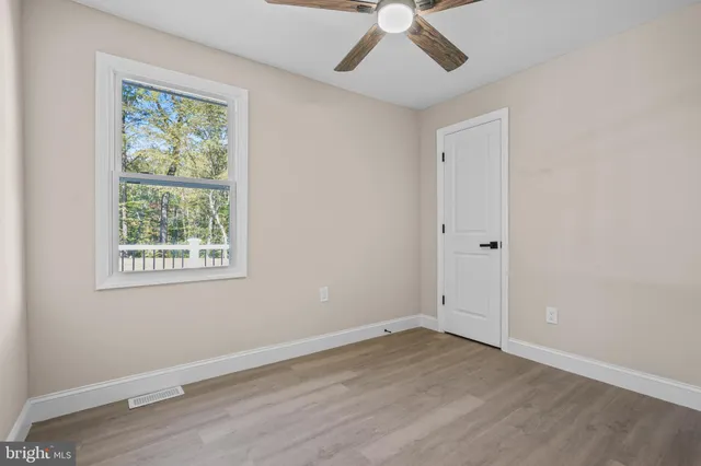 an empty room with wooden floor chandelier fan and windows