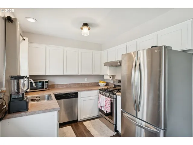 a kitchen with stainless steel appliances a refrigerator a sink a stove and white cabinets