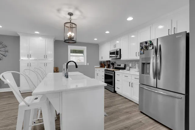 a kitchen with stainless steel appliances a refrigerator a stove a sink dishwasher a dining table and chairs with wooden floor