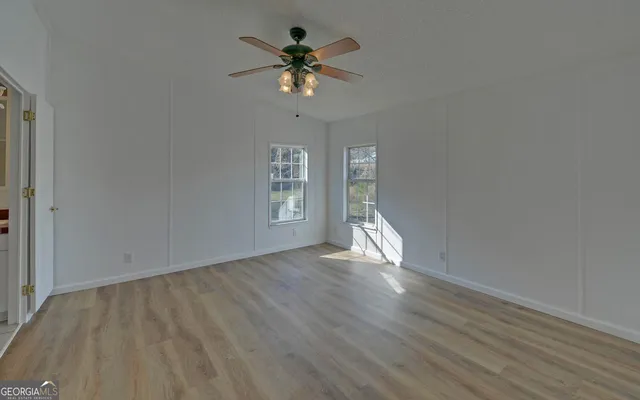an empty room with wooden floor chandelier fan and windows