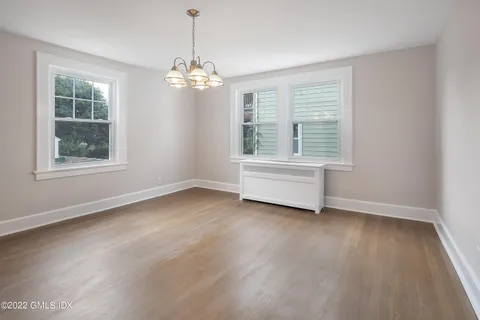 an empty room with wooden floor chandelier and windows