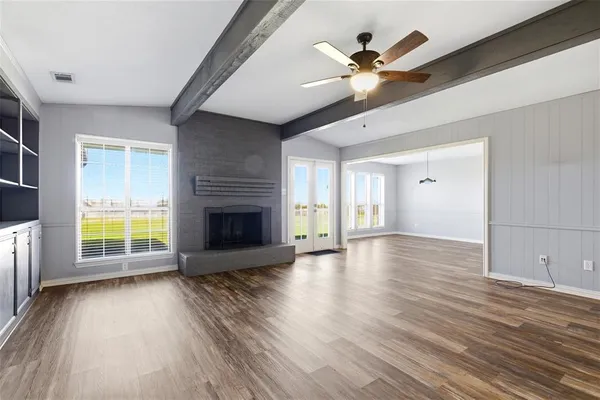 an empty room with wooden floor a ceiling fan a fireplace and windows