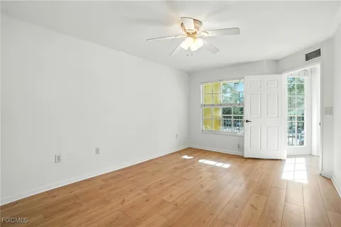 an empty room with wooden floor chandelier fan and windows