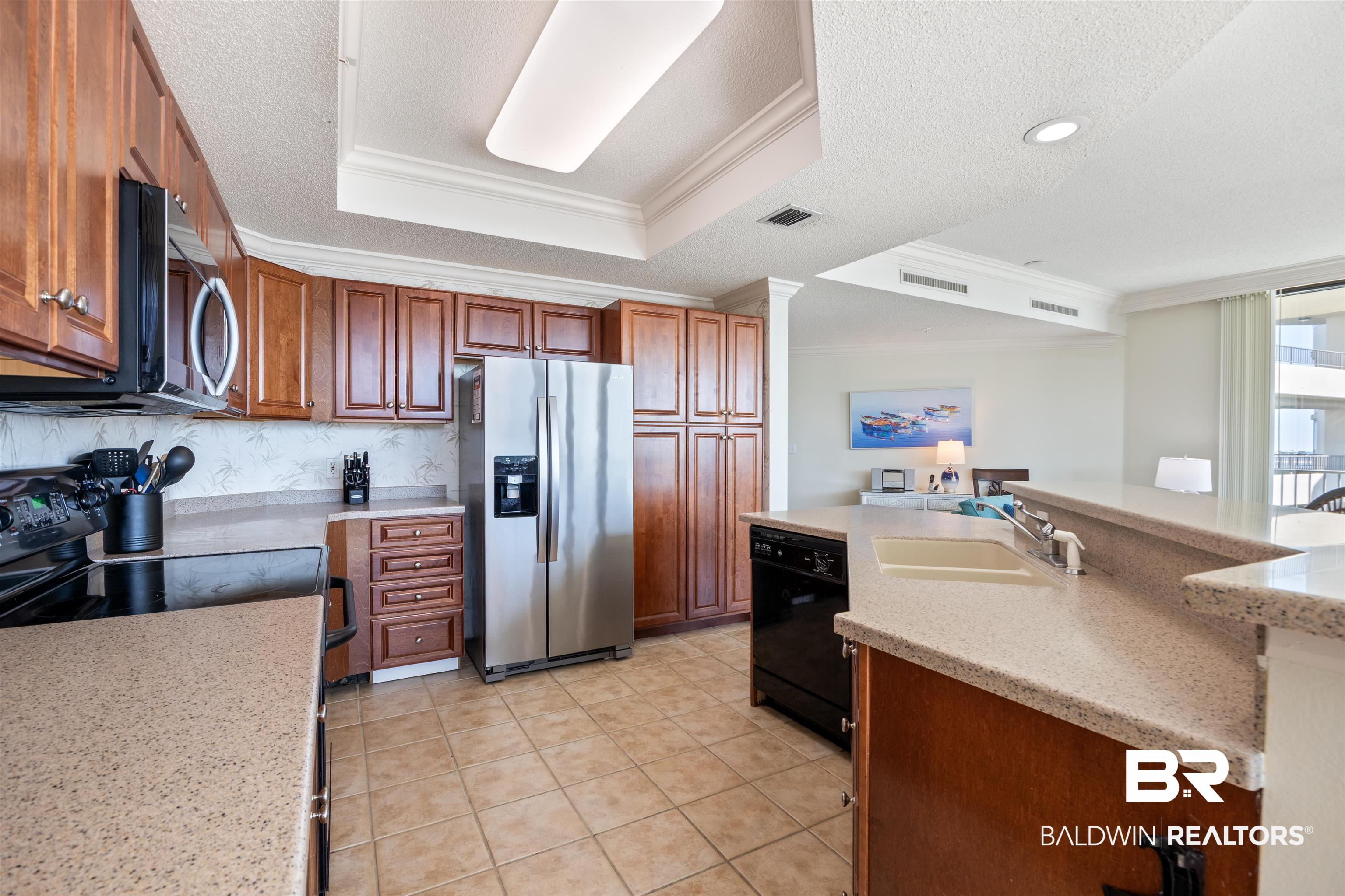 27580 Canal Road, Unit 1431 Orange Beach, AL 36561 - Photo 18 of 73 Kitchen featuring ornamental molding, a raised ceiling, black appliances, a textured ceiling, and a kitchen island with sink