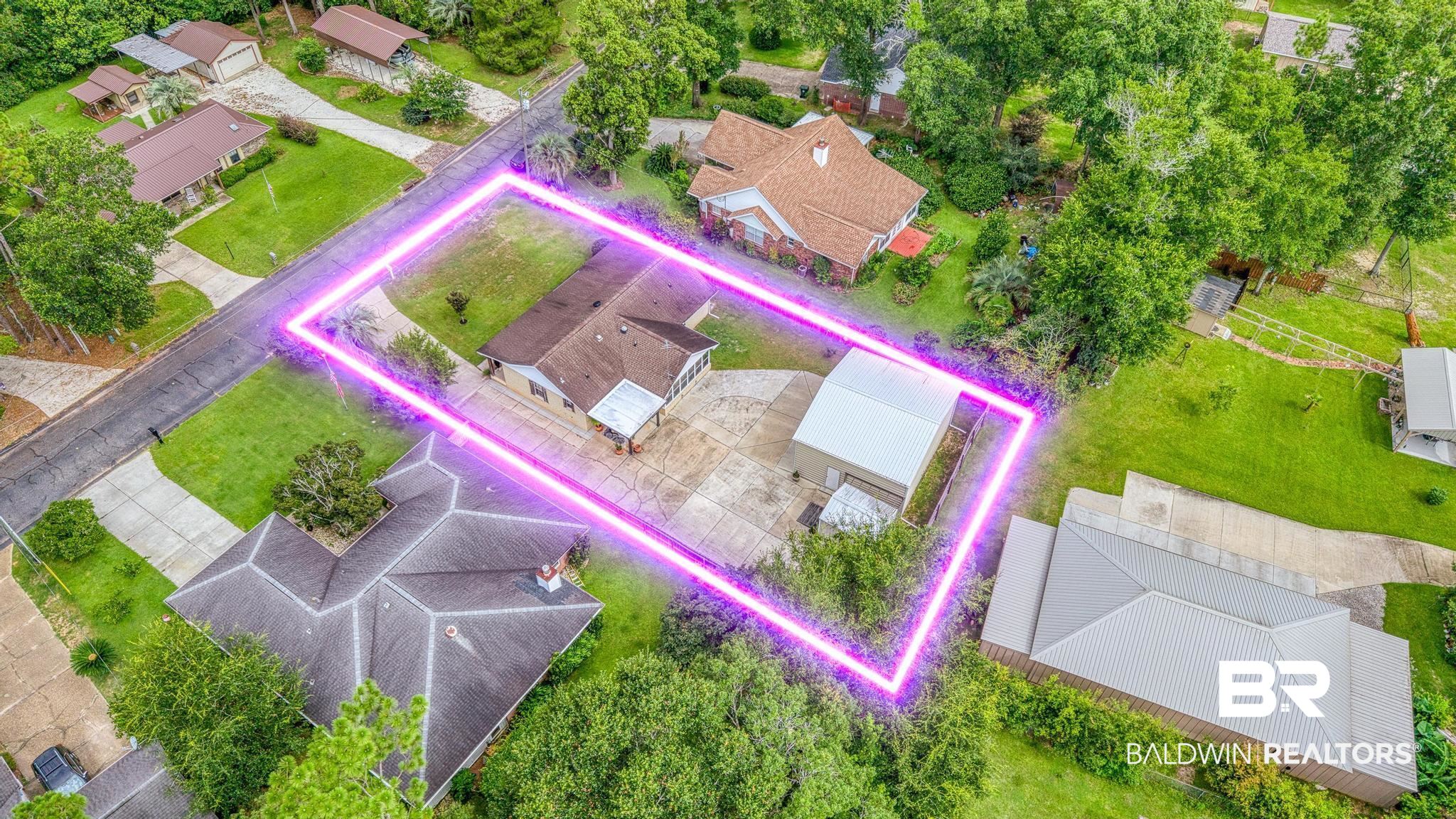 2808 Pine Ridge Drive Lillian, AL 36549 - Photo 4 of 47 Aerial view of a residential property featuring a single-story home with a brown shingle roof, an expansive concrete driveway, and a detached metal-roofed outbuilding