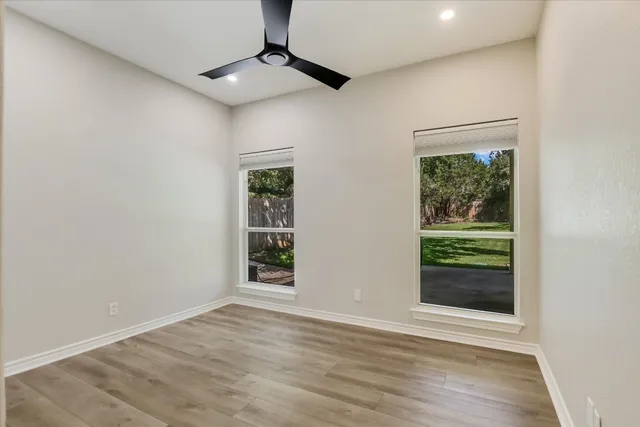 an empty room with wooden floor fan and windows