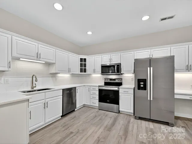 a kitchen with stainless steel appliances granite countertop a refrigerator a sink dishwasher a stove top oven a refrigerator with white cabinets and wooden floor