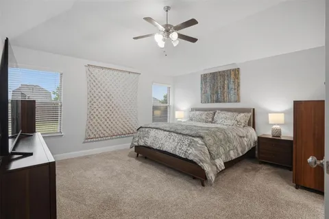 a spacious bedroom with a bed and a flat tv screen on the dresser