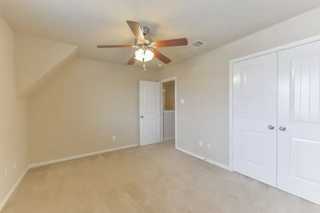 an empty room with a chandelier fan and closet area