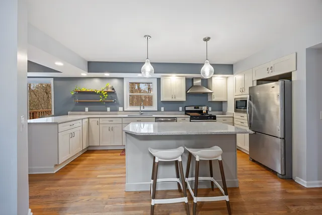 a kitchen with stainless steel appliances a refrigerator a sink dishwasher a stove and white cabinets with wooden floor