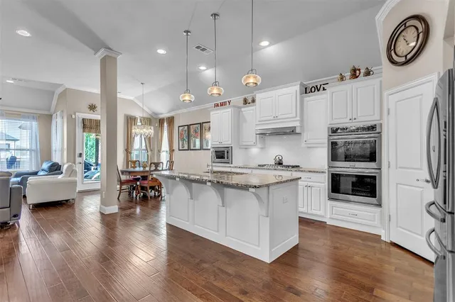 a kitchen with stainless steel appliances granite countertop a stove top oven a refrigerator a sink and a dining table with wooden floor