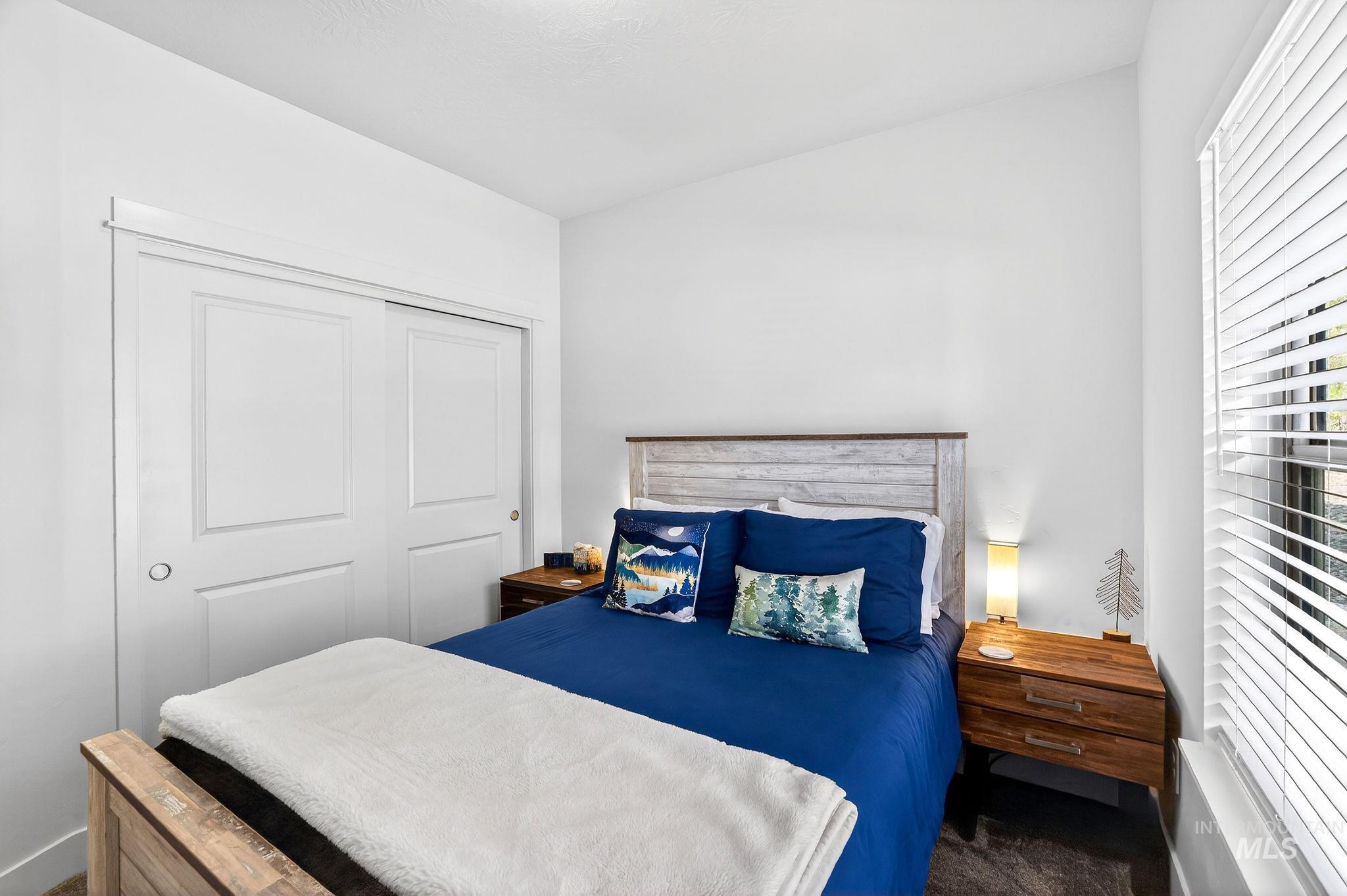 311 Broken Ridge Way McCall, ID 83638 - Photo 15 of 44 Vaulted ceiling bedroom featuring a wood-finish bed frame with a contrasting headboard, a built-in sliding closet with panel doors, and a window with horizontal blinds