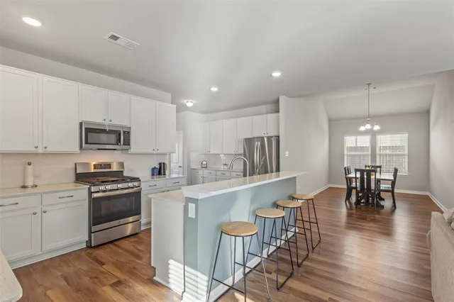 a kitchen with stainless steel appliances granite countertop a stove top oven a sink dishwasher a dining table and chairs with wooden floor