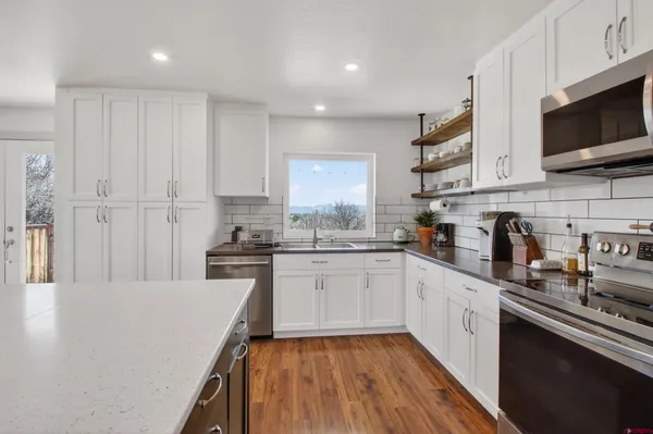 a kitchen with granite countertop a sink dishwasher stove and white cabinets with wooden floor