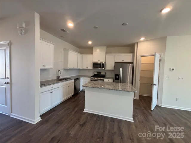 a kitchen with stainless steel appliances granite countertop a refrigerator a sink dishwasher a stove and white countertops with wooden floor