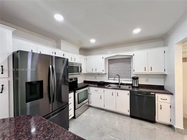 a kitchen with granite countertop a refrigerator sink and white cabinets