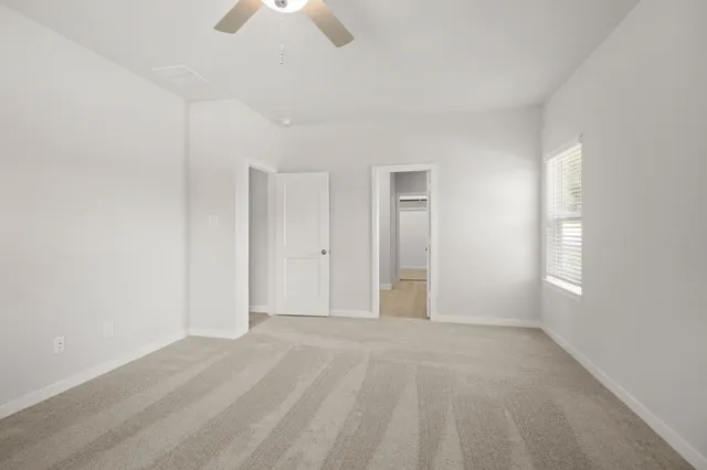 an empty room with chandelier fan and windows