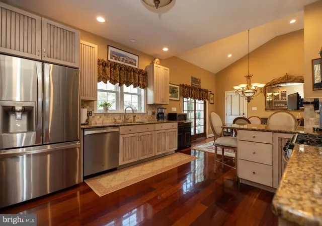 a kitchen with stainless steel appliances kitchen island granite countertop a refrigerator a stove a sink dishwasher and white cabinets with wooden floor