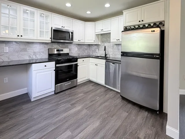 a kitchen with stainless steel appliances granite countertop a refrigerator stove a sink and white cabinets with wooden floor