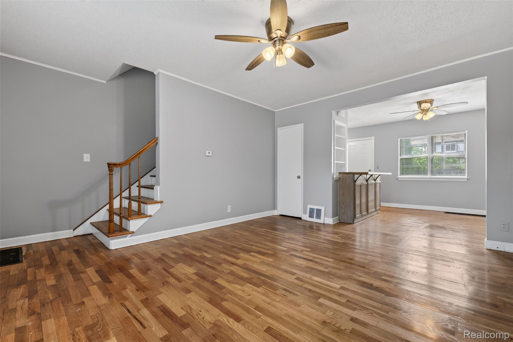 Hardwood flooring throughout, featuring a staircase with wood newel posts and railings, and ceiling fans with integrated lighting