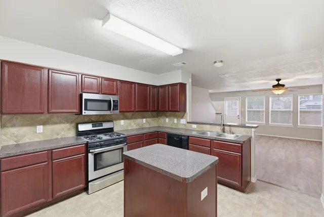 a kitchen with kitchen island granite countertop wooden cabinets a stove a sink and a oven with wooden floor