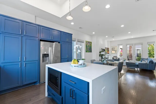 a room with stainless steel appliances kitchen island granite countertop a refrigerator a sink dishwasher a dining table and chairs with wooden floor