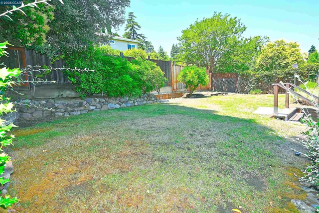 a view of a backyard with table and chairs potted plants and large tree