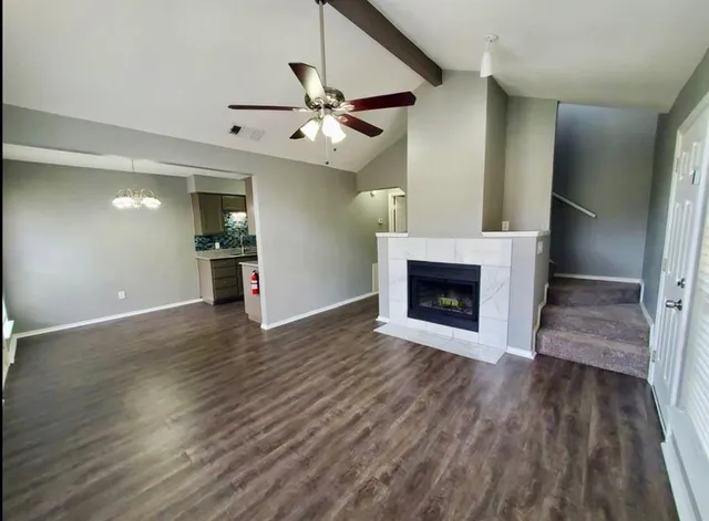an empty room with wooden floor a ceiling fan a fireplace and windows