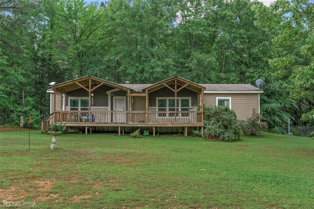 Single-story residence featuring light brown horizontal siding, a full-width wood deck with railings, and two covered porch areas with exposed wood rafter details