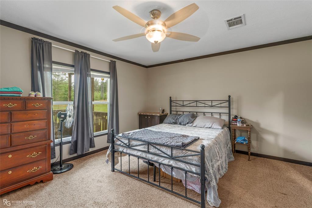 9489 Capps City Road Rodessa, LA 71069 - Photo 12 of 24 Carpeted room featuring a ceiling fan with integrated lighting, multiple windows with dark trim, light-toned wall paint, and dark crown molding