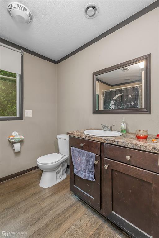 9489 Capps City Road Rodessa, LA 71069 - Photo 18 of 24 Bathroom featuring wood-finish flooring, a dark wood-tone vanity with a light-toned countertop, and a framed mirror
