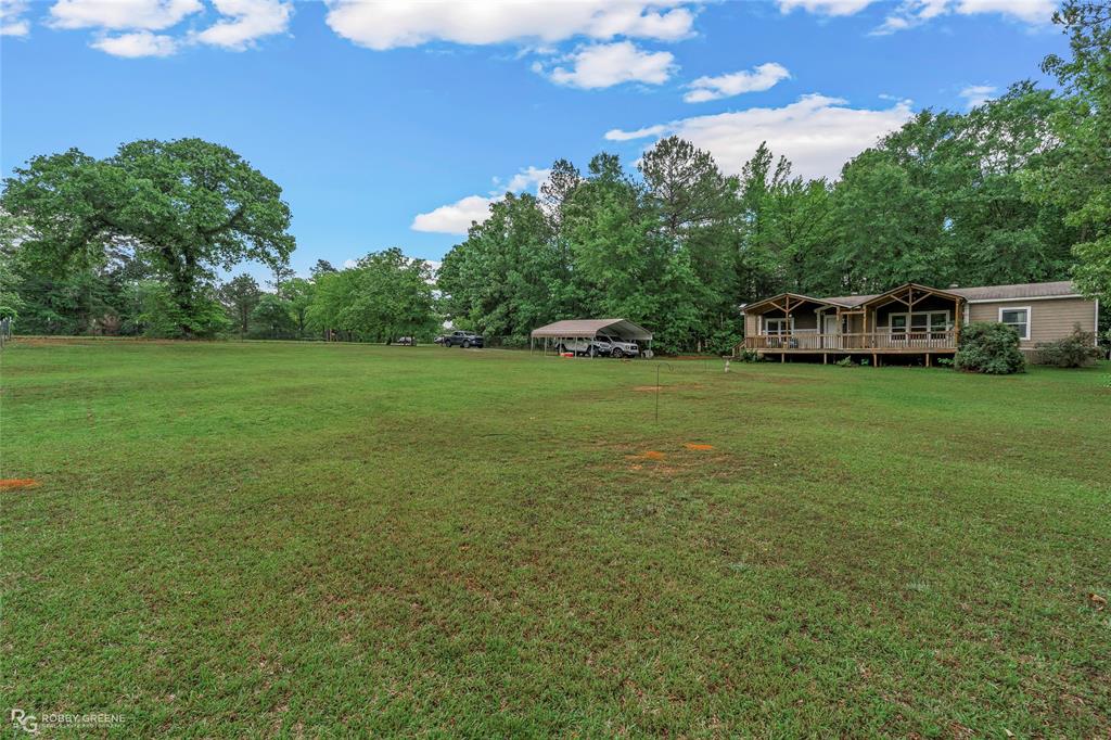 9489 Capps City Road Rodessa, LA 71069 - Photo 24 of 24 Expansive green lawn with a single-story residence featuring a covered front porch, an open carport, and surrounding mature trees