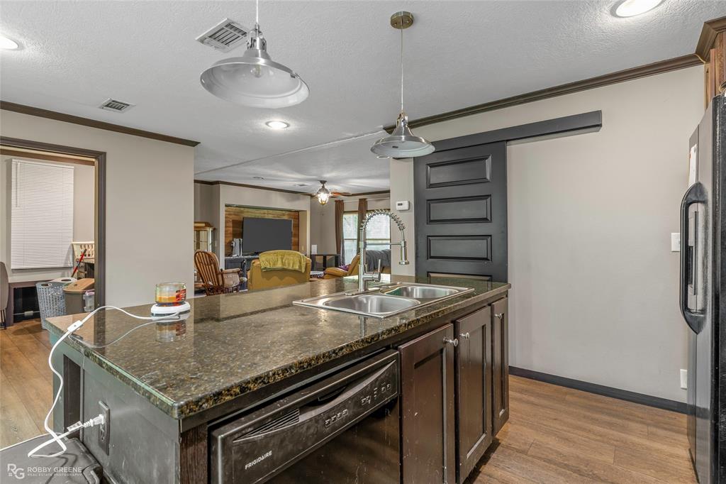 9489 Capps City Road Rodessa, LA 71069 - Photo 9 of 24 Kitchen island featuring a double basin sink, dark countertop, and integrated dishwasher