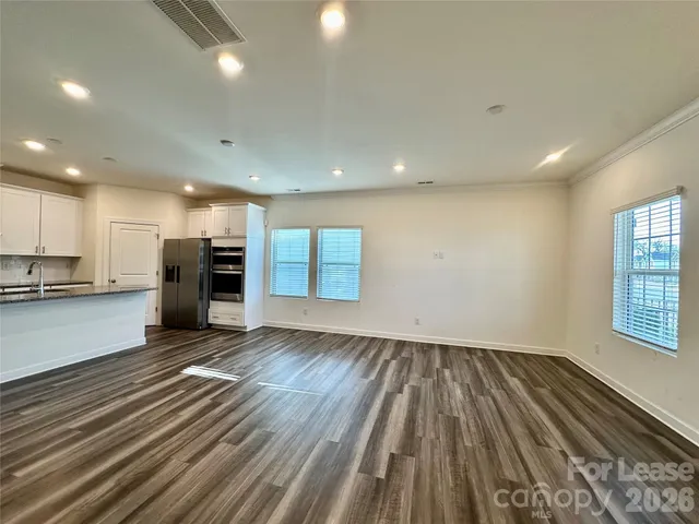 an empty room with wooden floor kitchen view and windows
