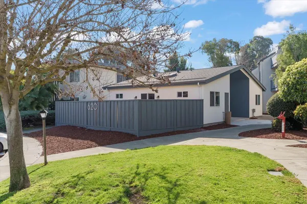 a view of a small yard in front of a house with large trees and wooden fence