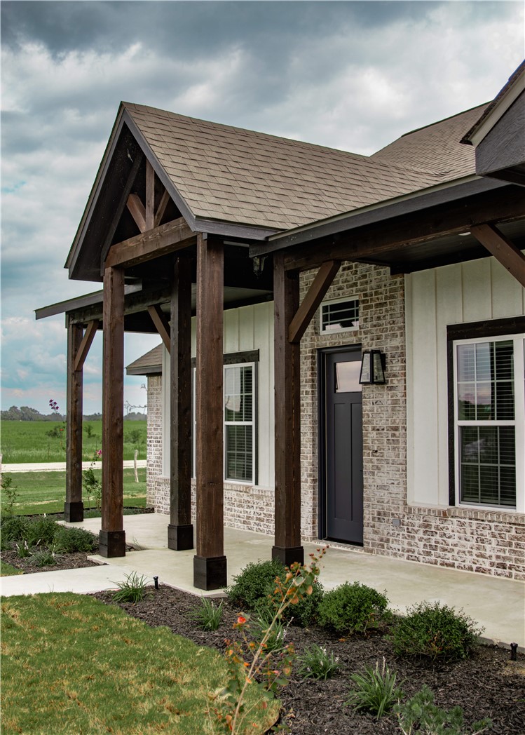 3201 Hunters Crossing Bryan, TX 77808 - Photo 5 of 40 Property entrance featuring board and batten siding, covered porch, a shingled roof, brick siding, and a yard