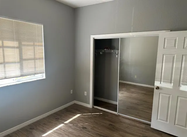 an empty room with wooden floor closet and windows