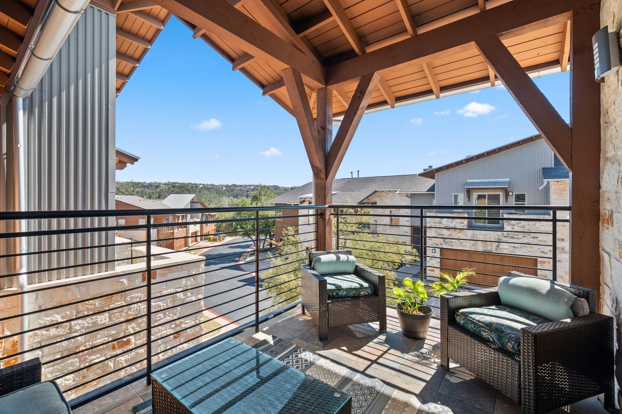 8110 Ranch Road 2222, Unit 92 Austin, TX 78730 - Photo 20 of 40 Covered balcony featuring exposed wood beams, a corrugated metal accent wall, stone wall siding, and horizontal metal railings