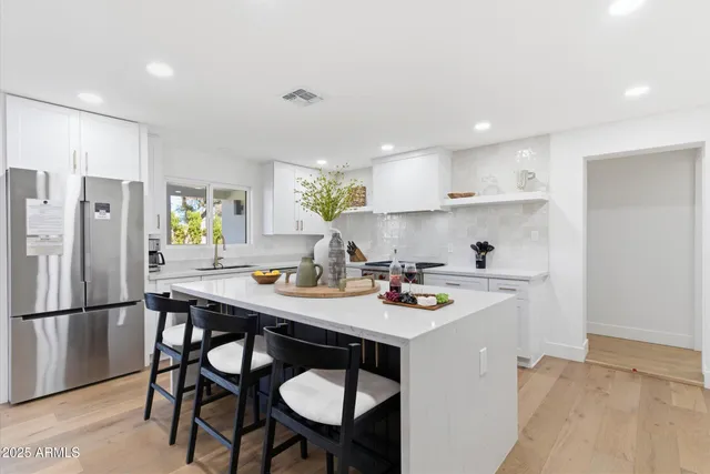 a kitchen with stainless steel appliances granite countertop a sink a stove a refrigerator white cabinets and chairs