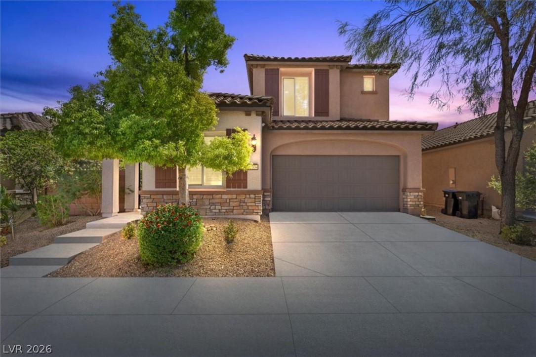 Twilight elevation shows the stone and stucco exterior with warm lighting, tile roof, and manicured desert landscaping.