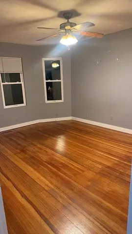 a view of an empty room with wooden floor and a ceiling fan