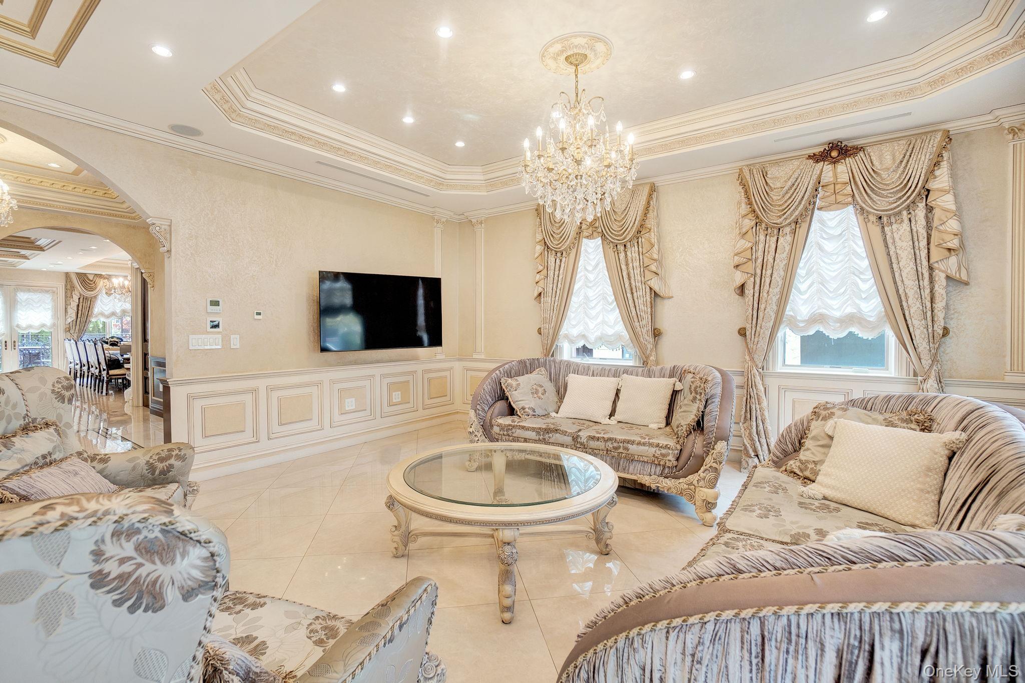 181-30 Tudor Road Queens, NY 11432 - Photo 11 of 46 Living room featuring a chandelier, arched walkways, crown molding, a raised ceiling, and a decorative wall