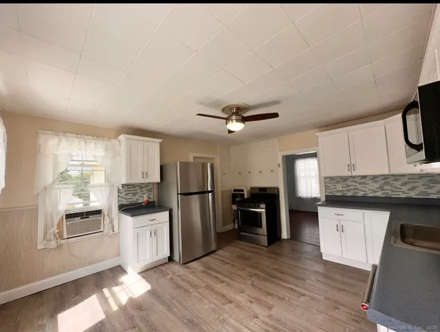 a kitchen with granite countertop a refrigerator oven a sink dishwasher and white cabinets with wooden floor