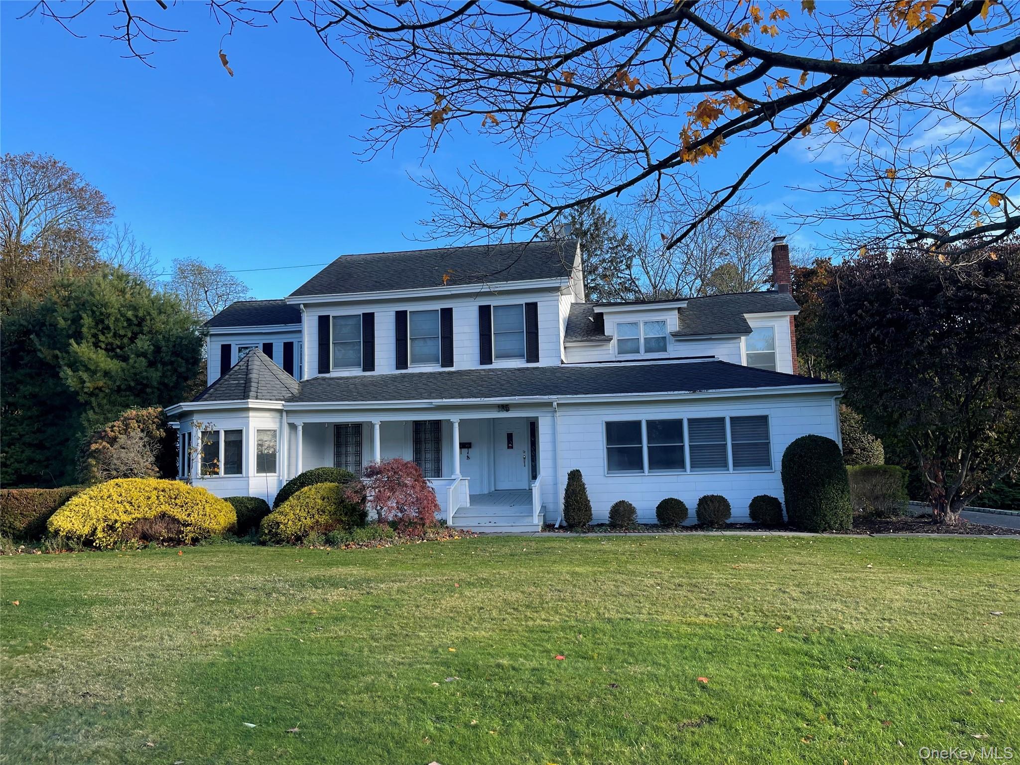 View of front of home featuring a front lawn, covered porch, roof with shingles, and a chimney