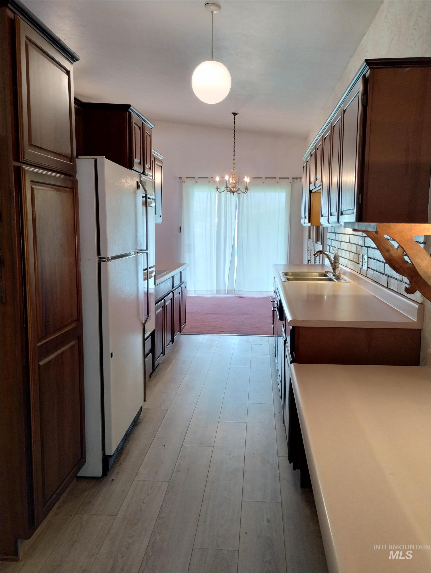 1298 East 2nd Street Weiser, ID 83672 - Photo 6 of 34 Kitchen featuring light countertops, pendant lighting, freestanding refrigerator, dark brown cabinets, and tasteful backsplash