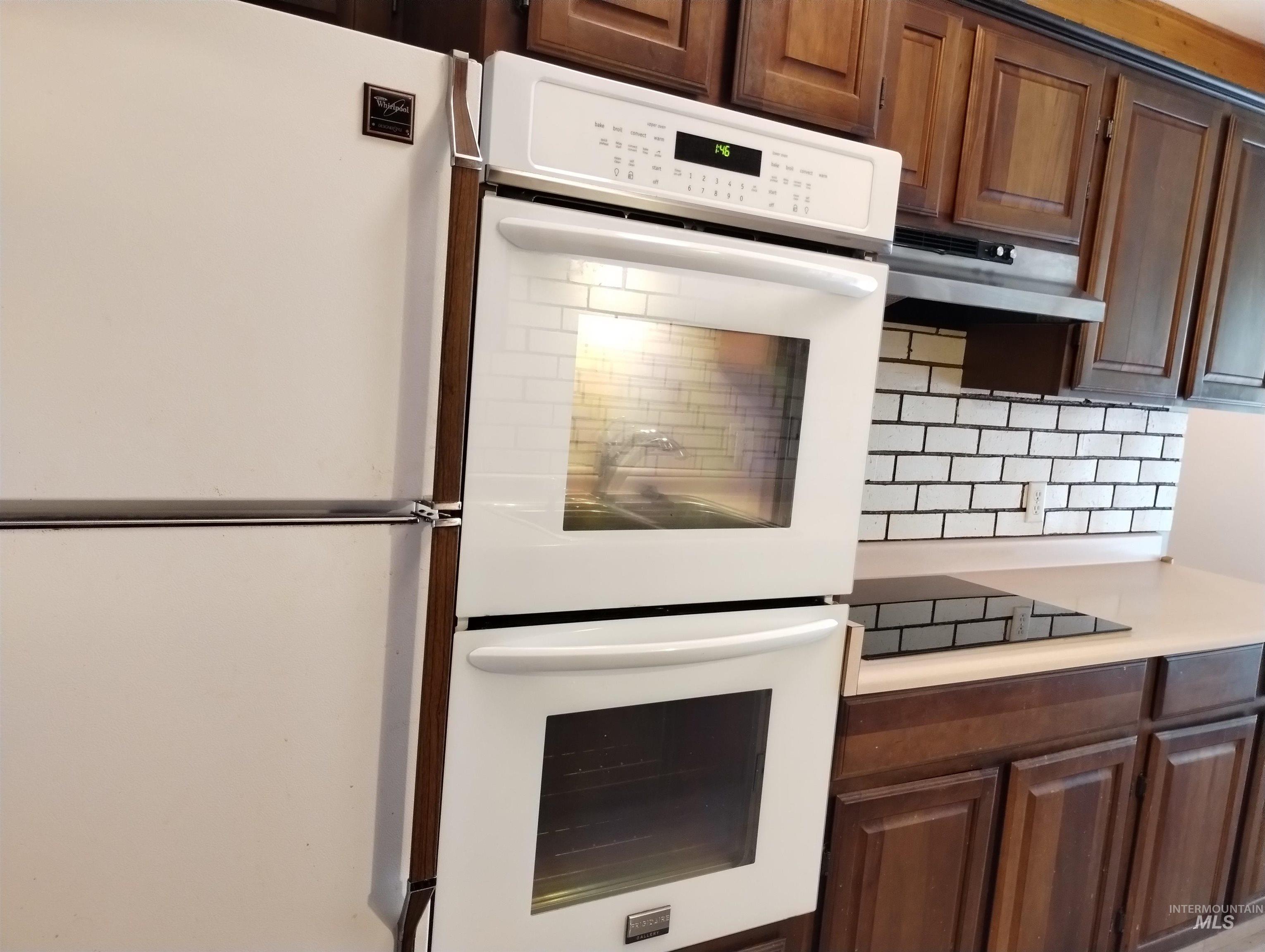 1298 East 2nd Street Weiser, ID 83672 - Photo 8 of 34 Kitchen featuring white appliances, light countertops, tasteful backsplash, under cabinet range hood, and dark brown cabinets