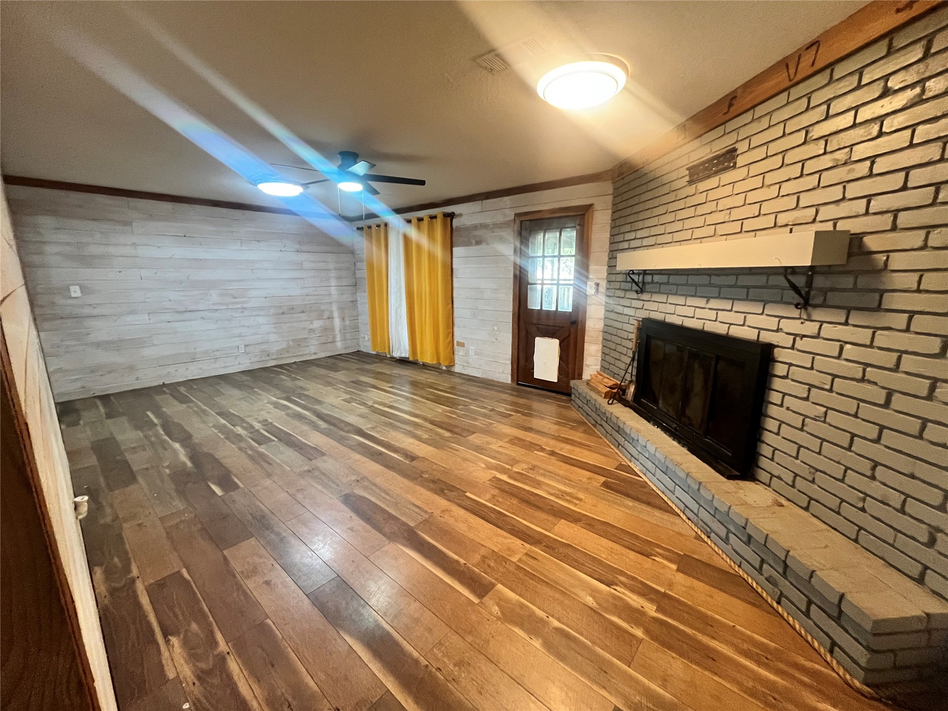 11131 215th Road Nowata, OK 74048 - Photo 15 of 47 From foyer, facing fireplace in living room, Back door is in view. Brick fireplace with hearth, wood-finish flooring, wood-paneled accent wall, and a ceiling fan with integrated lighting